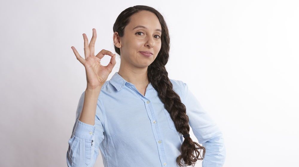junge Frau mit langem Zopf macht "OK"-Zeichen.